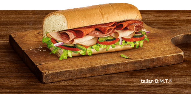 A delicious bacon, egg and cheese sandwich on freshly toasted flatbread OR A scrumptious Italian BMT sub on a wooden cutting board.